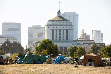 A homeless encampment frames the skyline of downtown Oakland, California, USA.