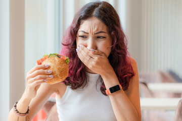 A girl eats a burger in a fast food cafe and feels nausea and heartburn. The concept of unhealthy...