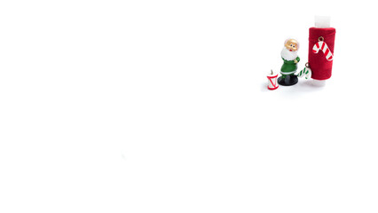 A red spool of sewing thread decorated with Christmas toys and a Santa Claus gnome on a white background.