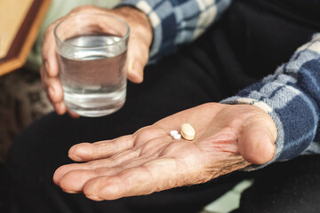 An elderly man holds pills and a glass of water in his hands. Taking pills to treat the disease