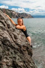 Woman swimsuit sea. Attractive blonde woman in a black swimsuit enjoying the sea air on the seashore around the rocks. Travel and vacation concept.