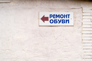 A plaque on the wall with an arrow and the text "Shoe Repair" in Europe with an inscription in Russian