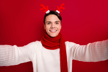 Selfie photo of positive guy wear deer horns toothy beaming smiliing take portrait cadre enjoy winter time spirit isolated on red color background