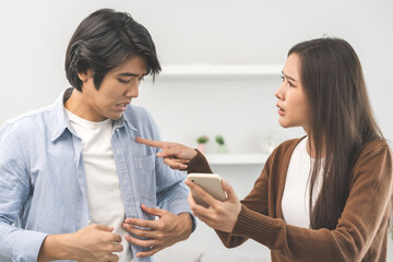 Infidelity, suspicion asian young couple love fight relationship, wife holding cellphone, smartphone cheating on phone, scolding husband about mistrust, distrust and jealousy at home.