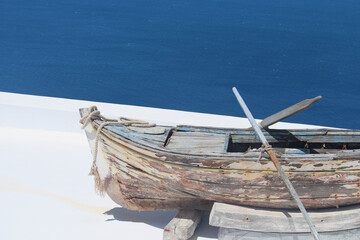 Fototapeta na wymiar Wooden boat with oars, hand painted and positioned outside a terrace overlooking the sea in Santorini.