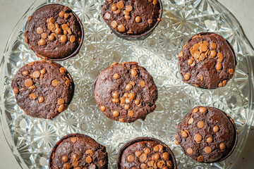 Overhead view of homemade muffins with chocolate chips cakes on a glass plate. Directly above close-up macrophotography with sunlight shining and shadows from the side.