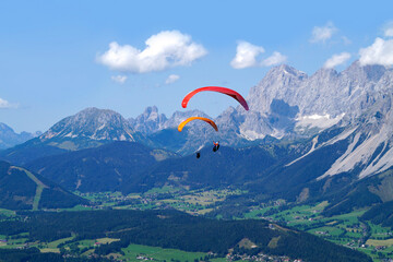 paragliders flying over the vast alpine valley surrounded by the Austrian Alps of the Schladming-Dachstein region on a sunny summer day (Schladming, Austria)