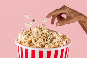 black male hand reaching Pop corn bucket on pink background with hand