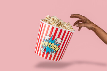 black male hand reaching Pop corn bucket on pink background with hand