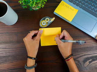 women write in yellow notes, mock up yellow notes. Women's hands write notes on yellow note paper in the background of the office desk workspace from the top view.