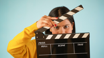 Closeup of a beautiful young Asian Indian woman standing holding clapperboard, clapper board used...