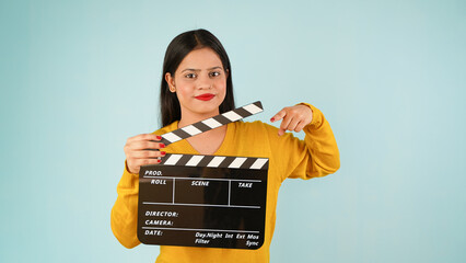 Beautiful young Asian Indian woman standing holding clapperboard, pointing index finger on clapper...