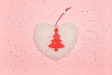 Artificial snow in the shape of a heart, and on it a wooden toy in the form of a Christmas tree. Minimalist Christmas concept.