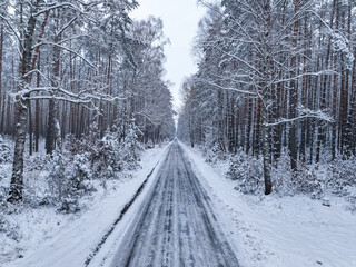 Flying above asphalt road and snowy forest in winter, Poland.