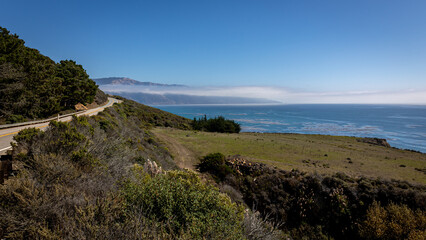 The beautiful west coast of California along Highway 1, with meadows and rocks, a blue sky and sea, with the remnants of fog in the distance