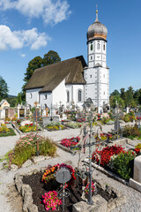 Die barocke katholische Kirche Mariä Schutz umgeben von Gräbern des Friedhofs von Fischbachau,...