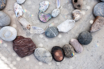 Stones, crystals, and seashells placed in a meditative mandala on a grey stone background sprinkled...