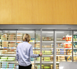  Man choosing frozen food from a supermarket freezer., reading product information
