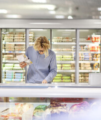  Man choosing frozen food from a supermarket freezer., reading product information