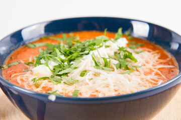 Italian tomato soup served with cream, mozzarella cheese and fresh parsley in a bowl, on a wooden pad on a white backround	
