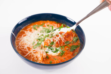 Italian tomato soup served with cream, mozzarella cheese and fresh parsley in a bowl, eaten with a spoon	
