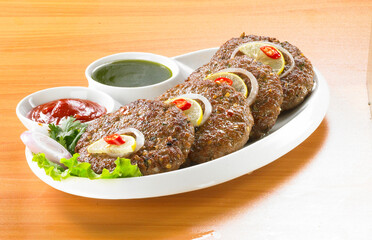 Spicy Pakistan Chapli Kebabs with fresh vegetables close up in the plate on the table.