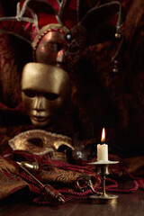 Burning candle in an old brass candlestick and carnival masks.