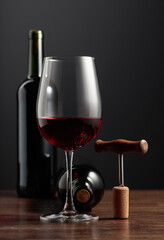 Red wine and corkscrew on a wooden table.