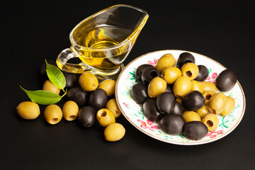Jug with olive oil, green and black olives on black background.