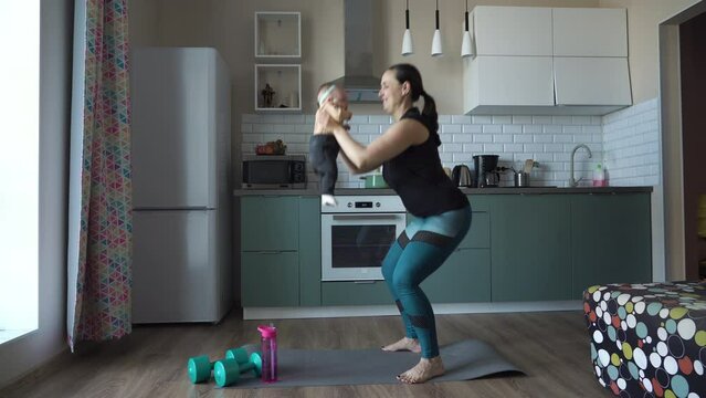 Sporty young mother is engaged with child in fitness exercises, woman doing squats in the kitchen