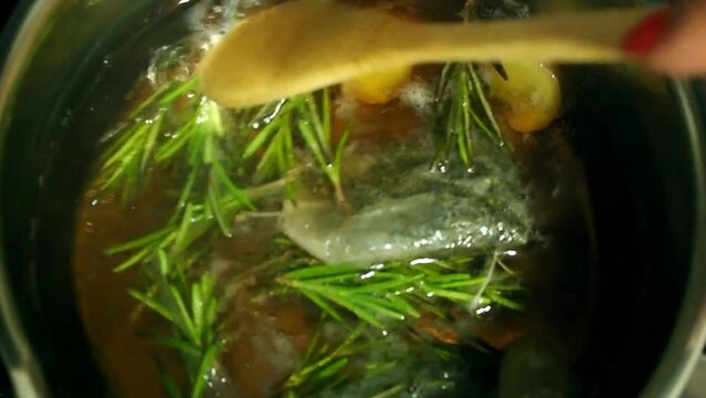 Pieces of ginger, a tea bag of green tea, rosemary sprigs are boiled in water. Stirring with a wooden spoon. The process of making infusion. Natural face or hair tonic.