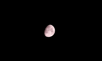 Moon on dark black sky background, shot from surface of earth with very long telephoto lens. Grey white moon glowing at clear sky.