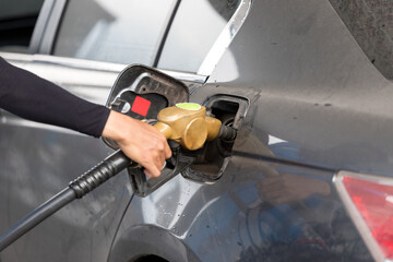 Hand holding a yellow refueling nozzle to refuel a car at a gas station