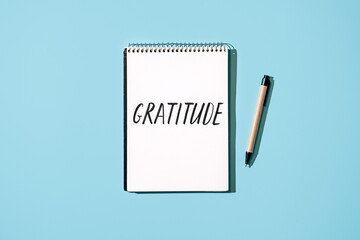 How to Practice Gratitude. Word Gratitude in open notebook on table. Notice good things, appreciate good things. Express gratitude to yourself. Word Gratitude in open notebook on blue background