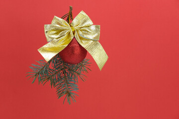Branch of Christmas tree is hanging with red glitter ball and golden bow on red shiny background....