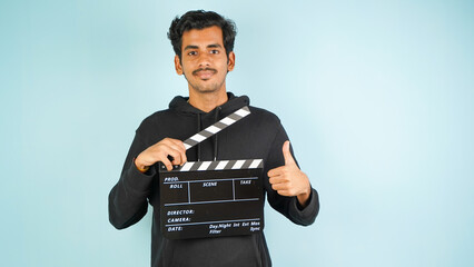 Young Asian Indian man standing holding clapperboard saying nice, clapper board used in film...