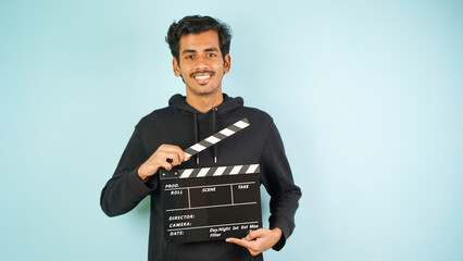 Cheerful Young Asian Indian man standing holding clapperboard, clapper board used in film making, isolated on colour background studio portrait