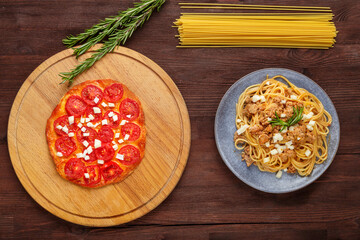 Pasta bolognese homemade on a plate and pizza with tomatoes on a wooden table.