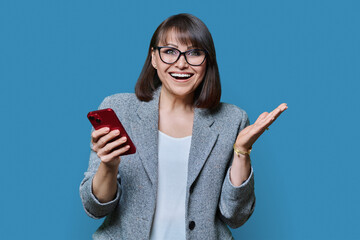 Portrait of middle aged business woman with phone on blue background