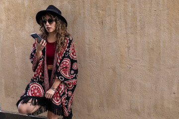Fototapeta premium Young latina woman with curly hair, hat, sunglasses, talking on her cell phone