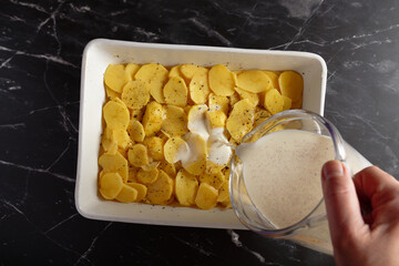 Raw potato slices for Gratin Dauphinois in baking dish, pour over cream milk.