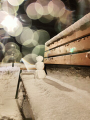 A small snowman on a bench covered with snow.