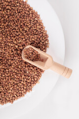 soft focus. a white plate with buckwheat in it. a small wooden spoon for spices. close-up.