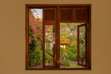 Window overlooking a tropical Asian garden with trees and plants, view from the inside.