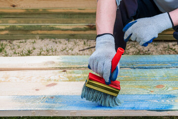 Wooden boards are painted with bright paint. Worker uses brush to paint boards.