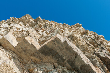 Stone cliff with many rocks against background of blue sky without clouds. Textural background of stone rock against sky.