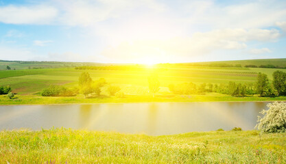 Meadow, lake, agricultural fields and sunrise on blue sky.