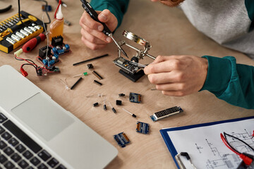 Technician solder microchip at table with laptop