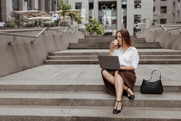 Young business woman sitting on a stairs with a laptop of the modern office building background 