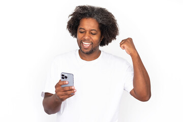Happy African American man using phone with clenched fist. Excited mature male model with dark curly hair in white T-shirt looking at screen, winning in game. Modern technology, advertising concept